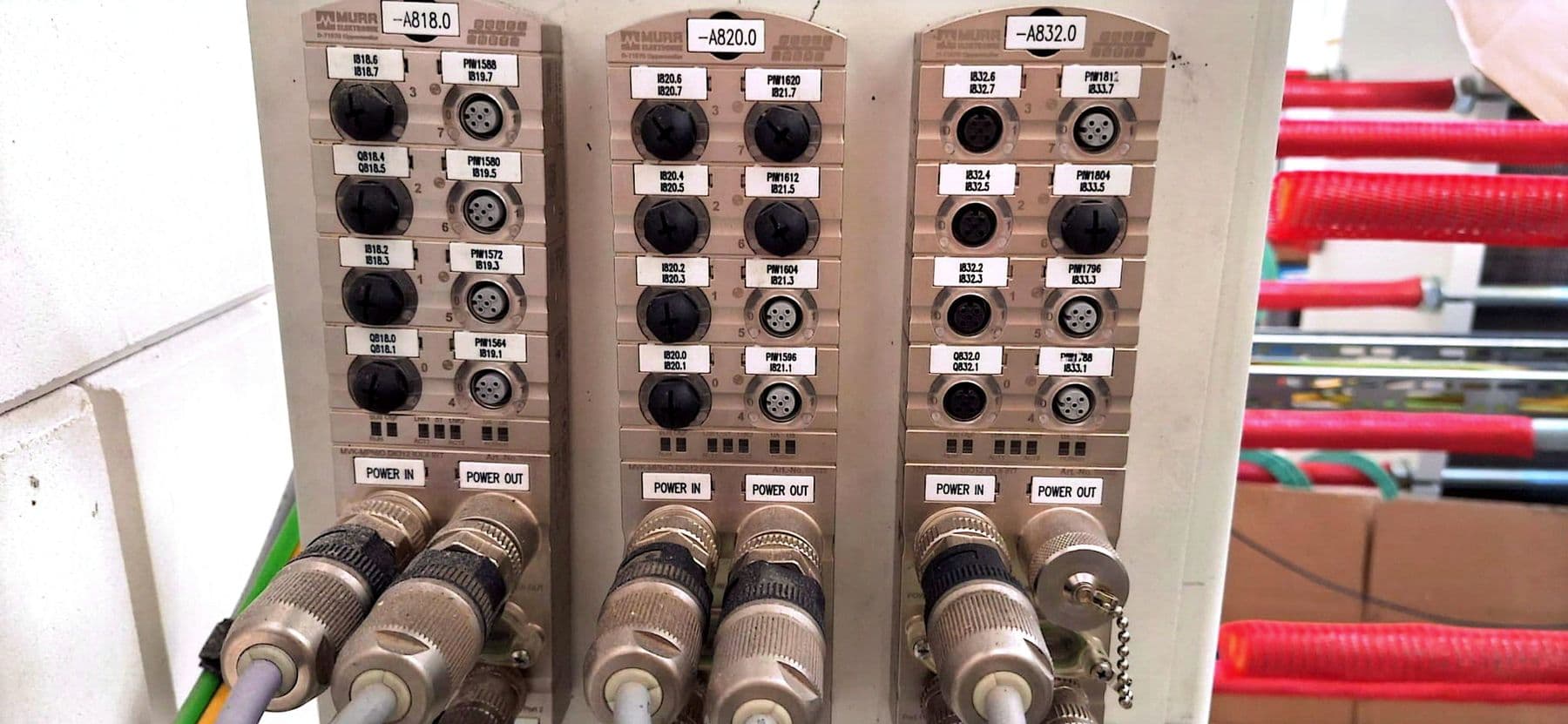 Drei Feldbusmodule mit M12-Buchsen, Beschriftungen und Rundsteckern, rechts rote Schutzschläuche