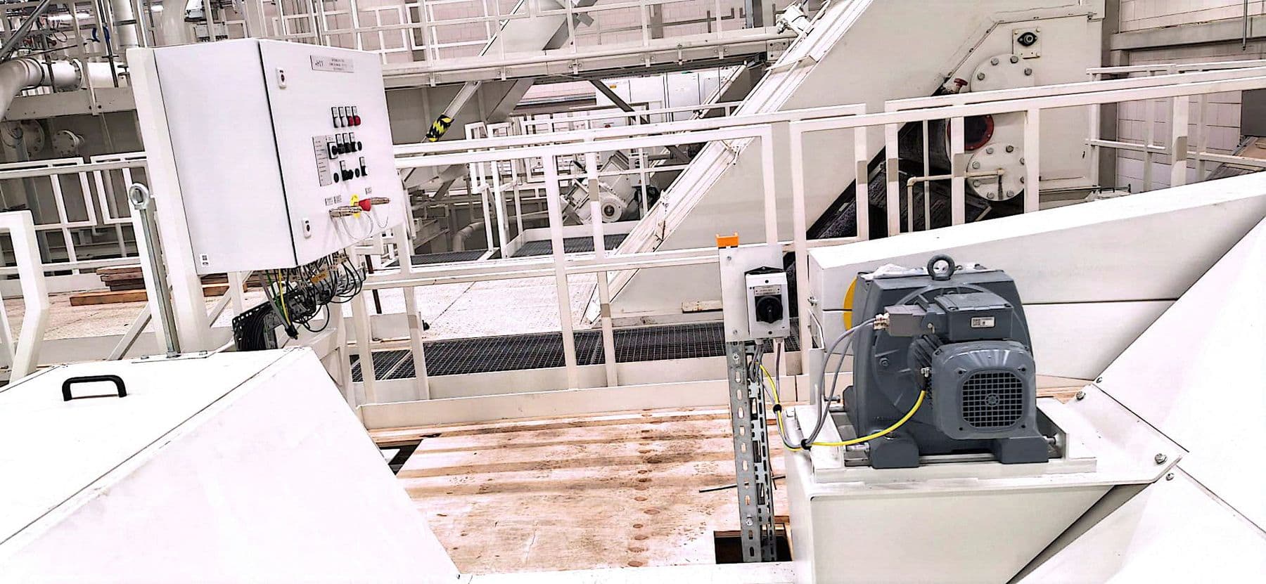 Getriebemotor mit angeschlossener Leitung und gelb-grünem Schutzleiter, daneben ein Schalter auf einer Stütze, im Hintergrund ein Schaltkasten
