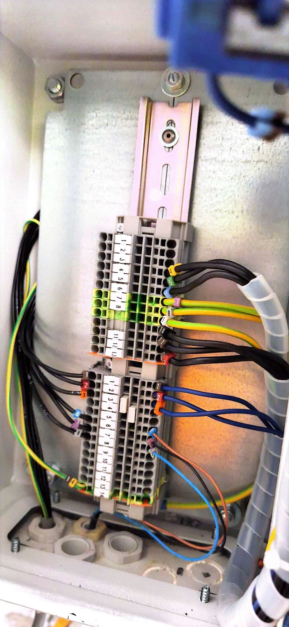 Geöffneter Anschlusskasten mit Hutschiene, Reihenklemmen und farbig gekennzeichneten Adern, rechts ein Spiralschlauch