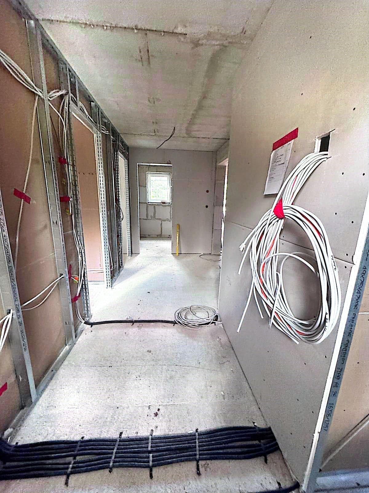 Flur im Trockenbau mit aufgerollten weißen Leitungen an der Wand und gebündelten schwarzen Kabeln am Boden