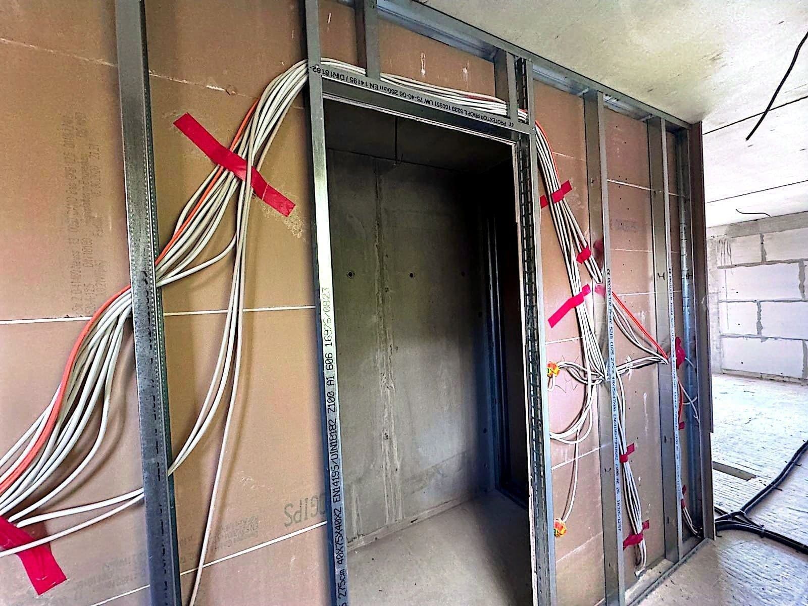 Türöffnung im Trockenbau mit Metallprofilen, weißen und orangeroten Leitungen und roten Klebebandmarkierungen