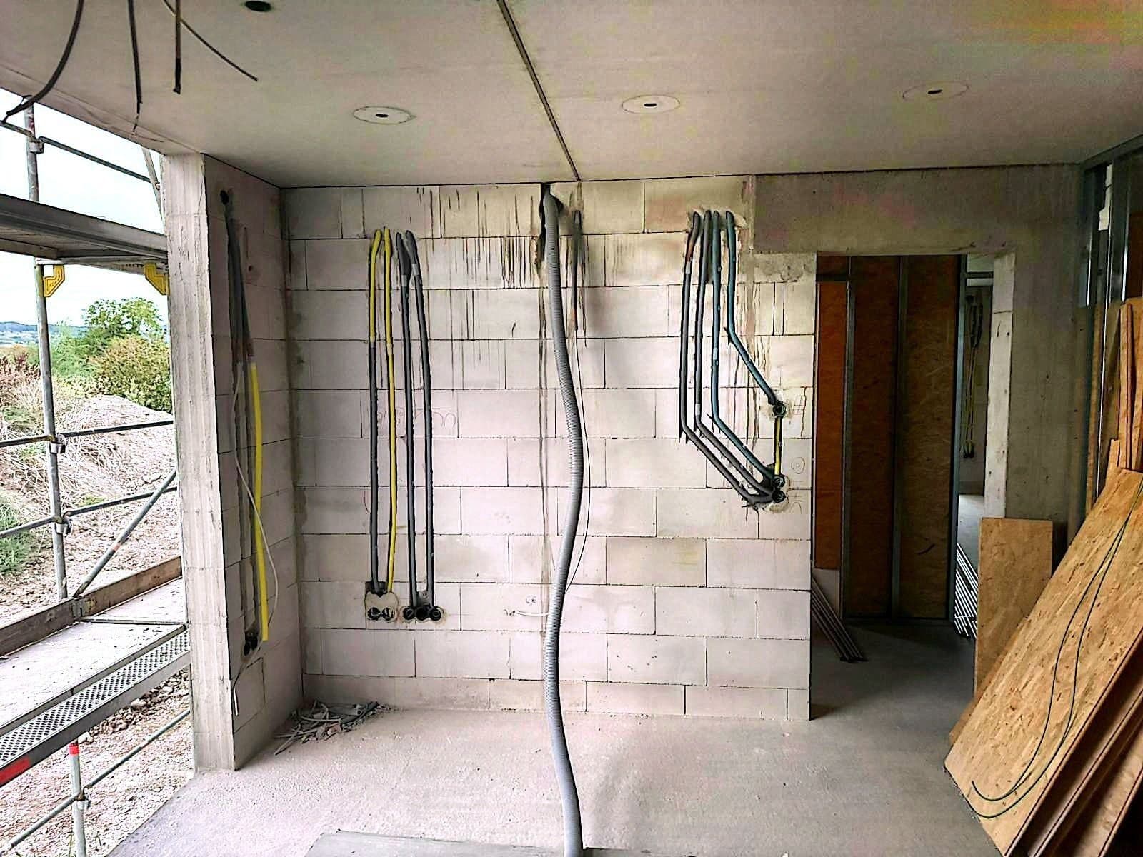 Rohbauraum mit Leerrohrbögen und gelben Leitungen an der Wand, links ein Gerüst und ein Fenster