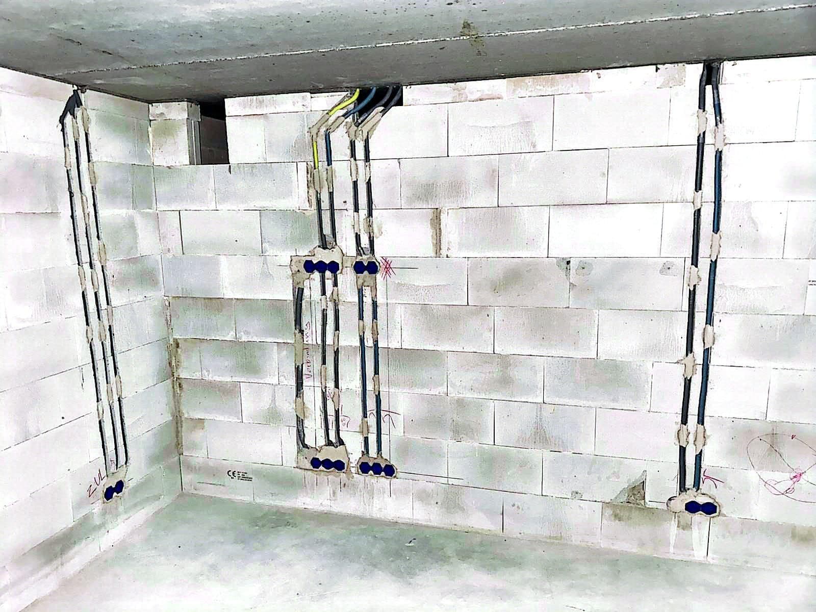 Mauerwerkswand mit senkrechten Leitungswegen, dunklen Kabeln und blauen Installationsdosen